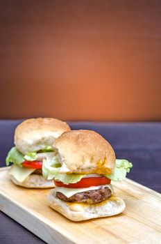 Delicious homemade gourmet cheese burgers made from beef with fresh ingredients placed on wooden platters