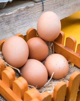 Brown chicken eggs leaning on straw in wooden basket.