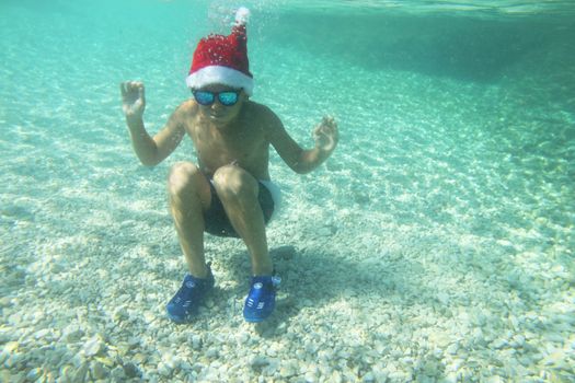 Boy in Santa Claus hat swimming underwater in sea, Christmas vacation at sea concept