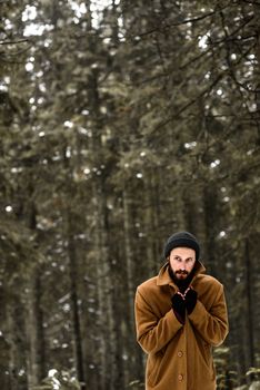 man in the winter forest is cold and in a brown coat and gloves