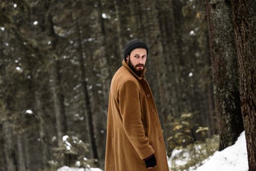 man in the winter forest is cold and in a brown coat and gloves