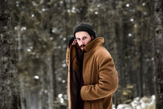 man in the winter forest is cold and in a brown coat and gloves