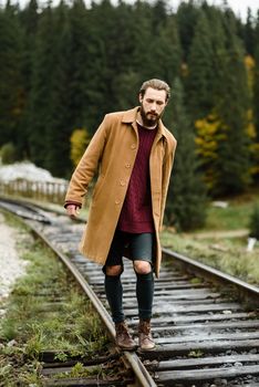 brutal bearded man walks on the tracks in the Carpathian mountains, in the background high firs