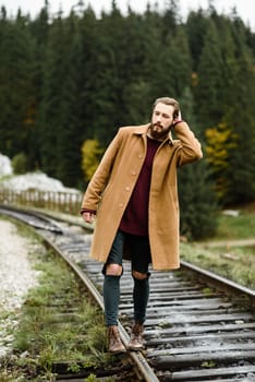 brutal bearded man walks on the tracks in the Carpathian mountains, in the background high firs