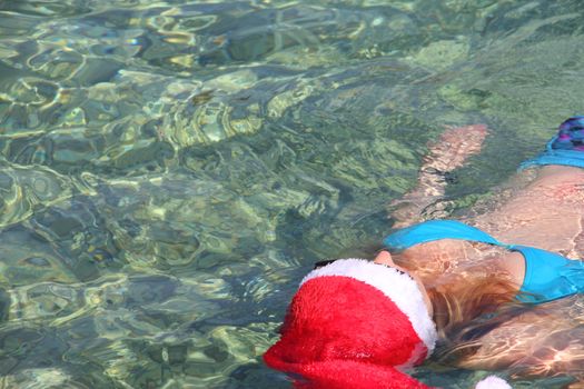 Woman in Santa Claus hat swimming in sea, Christmas vacation at sea concept