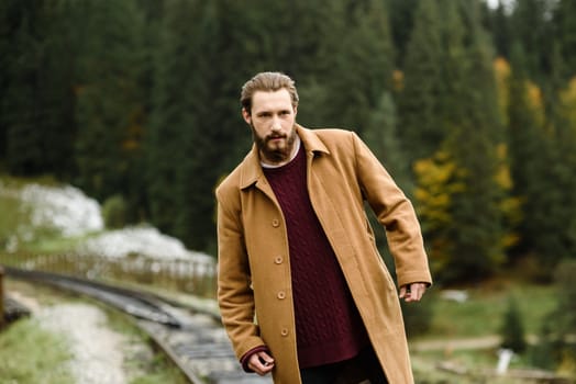 brutal bearded man walks on the tracks in the Carpathian mountains, in the background high firs