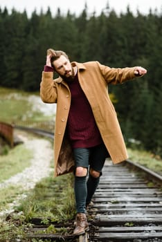 brutal bearded man walks on the tracks in the Carpathian mountains, in the background high firs