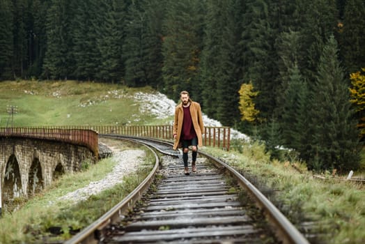 brutal bearded man walks on the tracks in the Carpathian mountains, in the background high firs