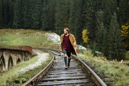 brutal bearded man walks on the tracks in the Carpathian mountains, in the background high firs