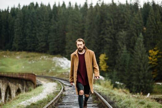 brutal bearded man walks on the tracks in the Carpathian mountains, in the background high firs