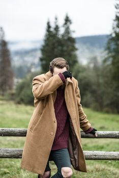 man in a brown coat and torn trousers was leaning against the fence