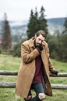 man in a brown coat and torn trousers was leaning against the fence