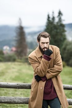 man in a brown coat and torn trousers was leaning against the fence