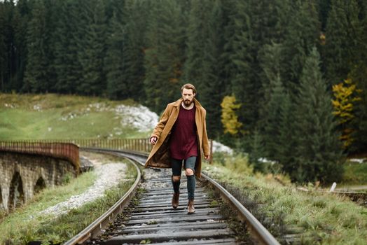 brutal bearded man walks on the tracks in the Carpathian mountains, in the background high firs