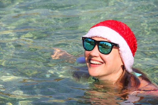 Woman in Santa Claus hat swimming in sea, Christmas vacation at sea concept