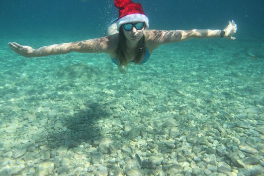 Woman in Santa Claus hat swimming underwater in sea, Christmas vacation at sea concept