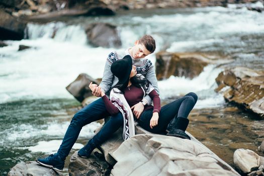 guy and girl in warm sweaters walking along a mountain river, love story