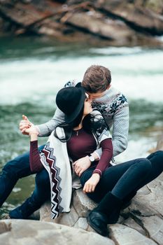 guy and girl in warm sweaters walking along a mountain river, love story