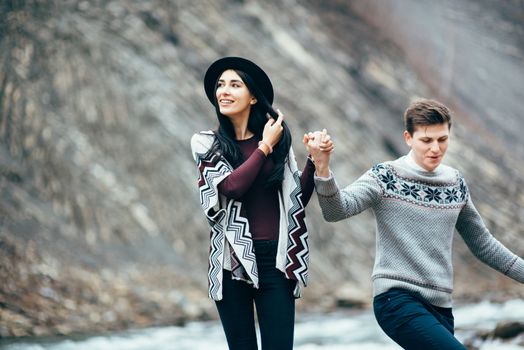 guy and girl in warm sweaters walking along a mountain river, love story