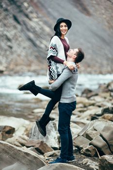 guy and girl in warm sweaters walking along a mountain river, love story