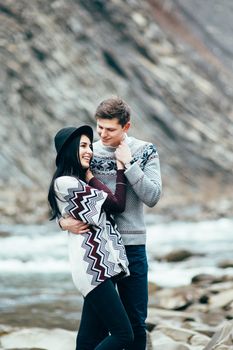 guy and girl in warm sweaters walking along a mountain river, love story