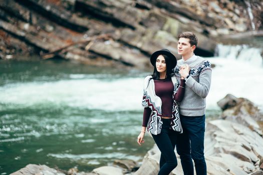 guy and girl in warm sweaters walking along a mountain river, love story