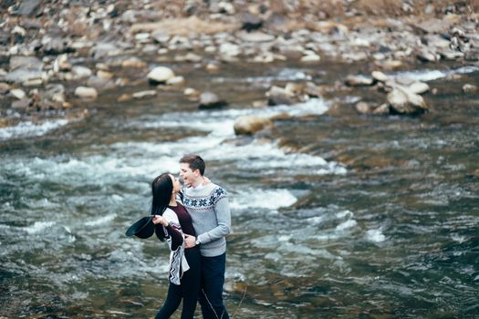 guy and girl in warm sweaters walking along a mountain river, love story