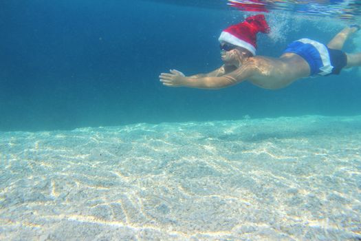 Boy in Santa Claus hat swimming underwater in sea, Christmas vacation at sea concept
