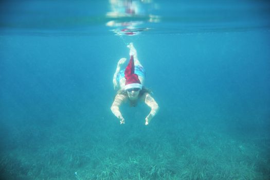 Woman in Santa Claus hat swimming underwater in sea, Christmas vacation at sea concept