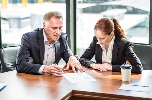 Mature business man and his young female assistant sitting at meeting table in office