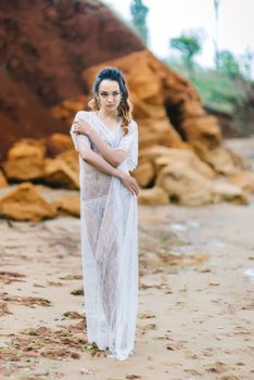 bride in her underwear and a dressing gown with a veil walks on the beach