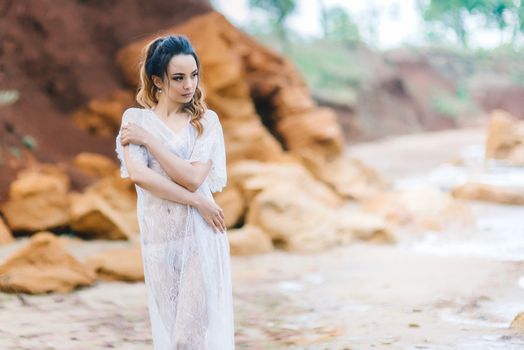 bride in her underwear and a dressing gown with a veil walks on the beach