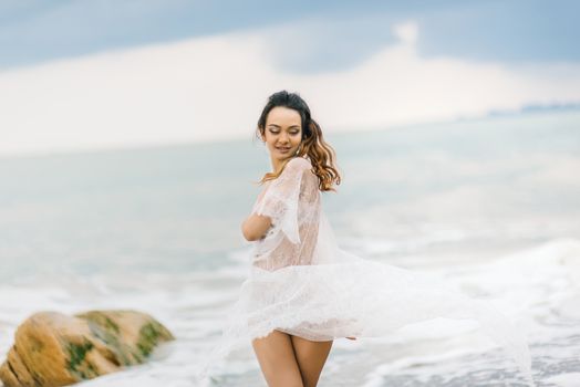 bride in her underwear and a dressing gown with a veil walks on the beach