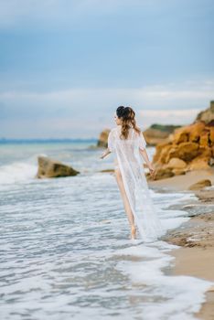 bride in her underwear and a dressing gown with a veil walks on the beach