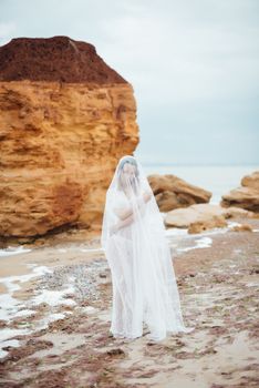 bride in her underwear and a dressing gown with a veil walks on the beach