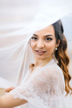 bride in her underwear and a dressing gown with a veil walks on the beach