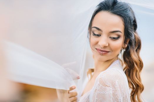 bride in her underwear and a dressing gown with a veil walks on the beach