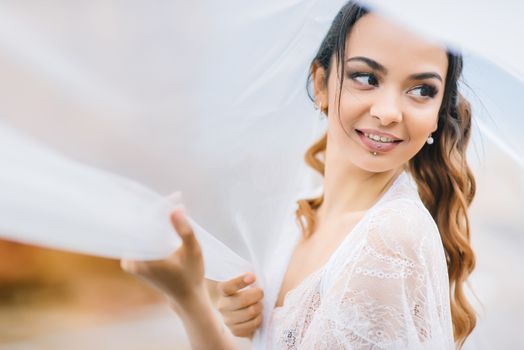 bride in her underwear and a dressing gown with a veil walks on the beach