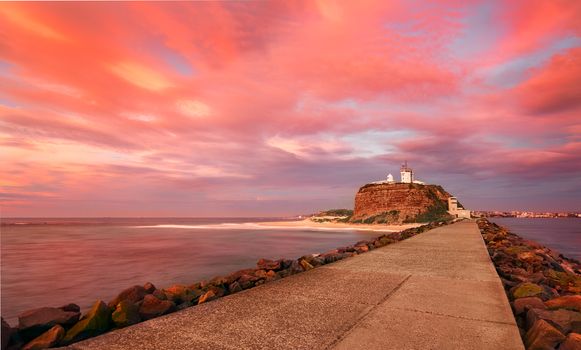 Nobbys Lighthouse under a blanket of clouds that coloured vividly at sunrise casting its glorious hues over the landscape