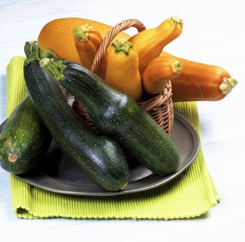 Arrangement of Green and Yellow Fresh Ripe Zucchini in Wicker Basket on Tin Plate and Napkin closeup on Wooden background
