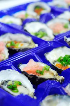 Close-up of fresh oysters mixed with ponzu sauce,ginger,vasabi sauce,and salmon caviar in trays in fish market