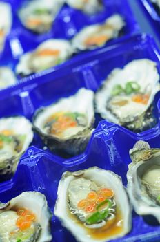 Close-up of fresh oysters mixed with ponzu sauce,ginger,vasabi sauce,and salmon caviar in trays in fish market