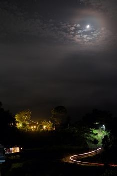 Night landscape with the moon, clouds and lighted buildings.