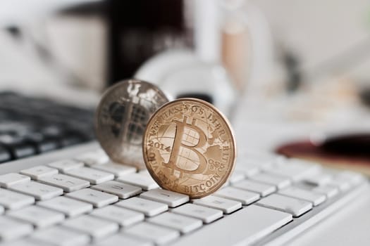Digital currency physical metal bitcoin coin on the white keyboard near glass ball.
