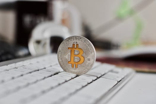 Digital currency physical metal bitcoin coin on the white keyboard near glass ball.