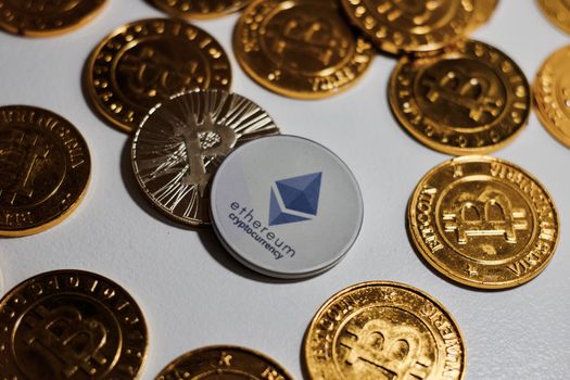 Digital currency physical grey Ethereum coin near gold bitcoins.