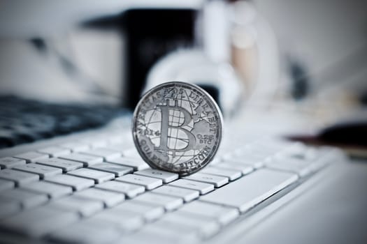 Digital currency physical metal bitcoin coin on the white keyboard near glass ball.