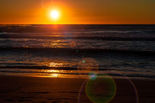 sunset on the beach in autumn with rough sea and lens flare