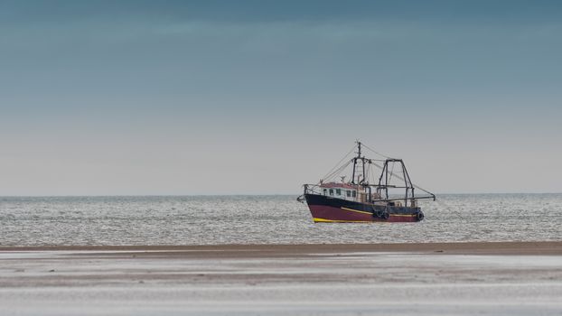 A small fishing trawler just off the seashore on the coast with its nets dropped in the water and very close to the shore