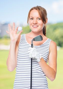 Golfer holding a golf club and showing a white ball on a background of golf courses